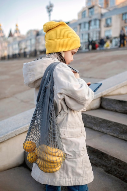 Preteen Mädchen sitzt auf Straßentreppe und SMS mit Smartphone auf dem Weg vom Einkaufen