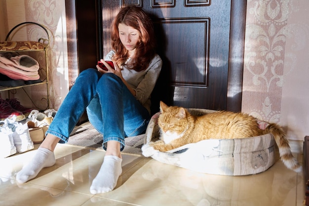 Preteen Mädchen sitzt zu Hause auf dem Boden mit Smartphone mit schlafender Hauskatze