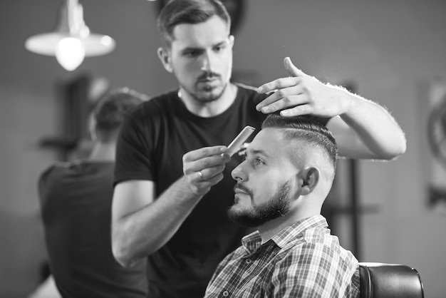 Preto e branco de um barbeiro profissional trabalhando para cortar o cabelo de seu cliente com uma tesoura