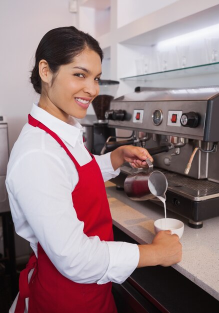 Pretty barista despejando leite em uma xícara de café