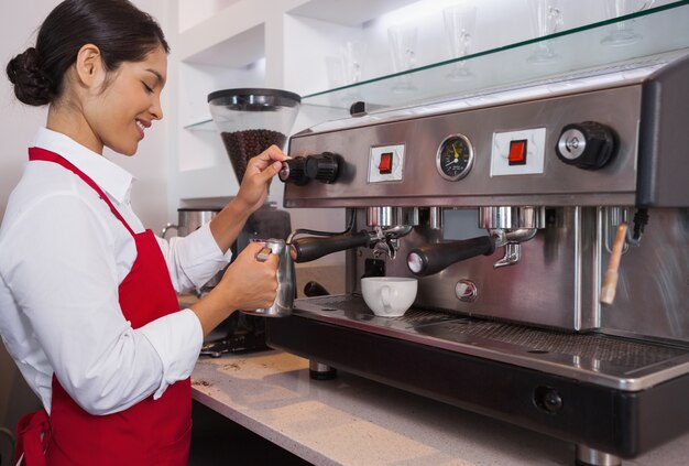 Pretty barista humeante jarra de leche en la máquina de café