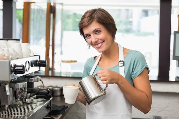 Pretty barista verter leche en una taza de café