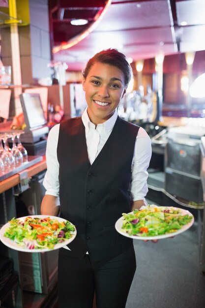 Pretty barmaid segurando pratos de saladas