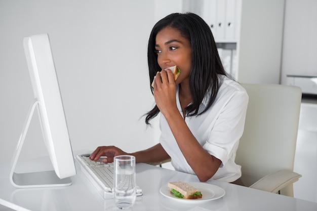 Pretty empresaria comiendo un sándwich en su escritorio