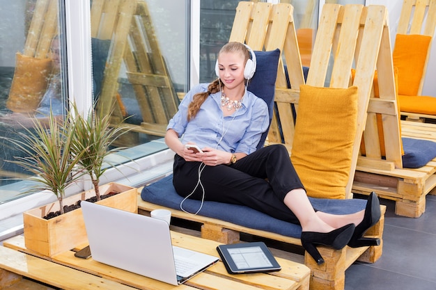 Pretty empresaria está escuchando música en loft moderno. Concepto de trabajo independiente, relax y ocio. Mujer de negocios. Freelancer en el centro de coworking está descansando.