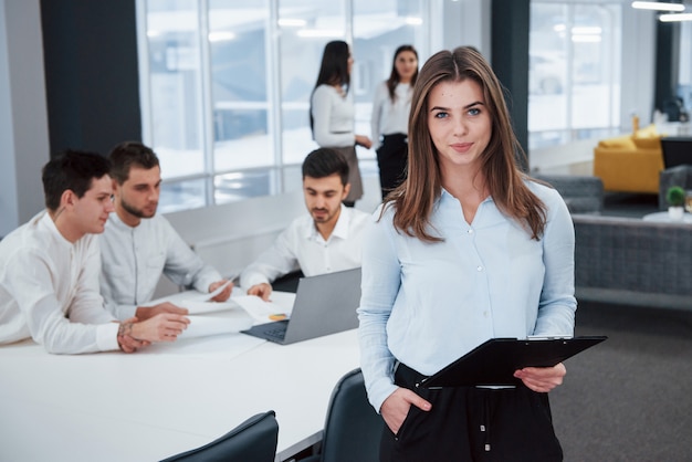 Pretty empresaria. Retrato de joven se encuentra en la oficina con empleados en el fondo