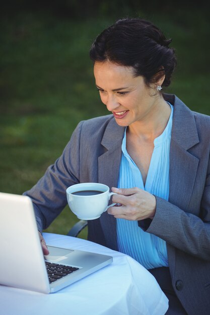 Pretty empresaria usando laptop y tomando un café