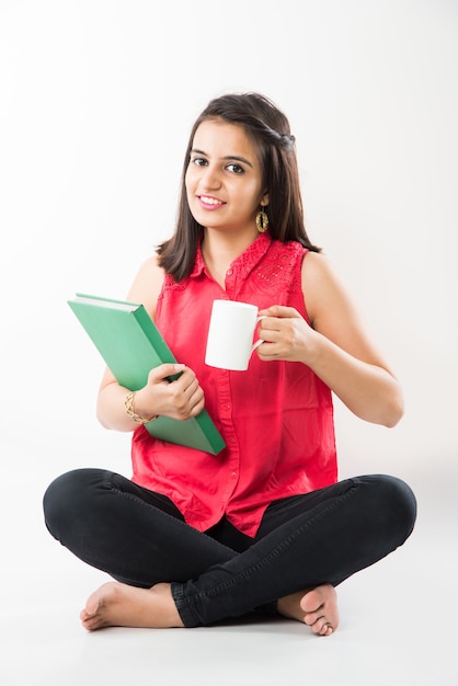 Pretty Indian Asian College Girl estudiando de libro mientras está sentado sobre fondo blanco.