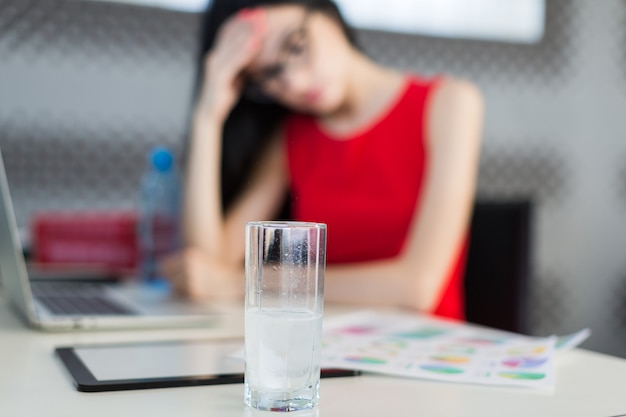 Pretty, jovem businesslady em vestido vermelho e óculos sentar à mesa e trabalhar