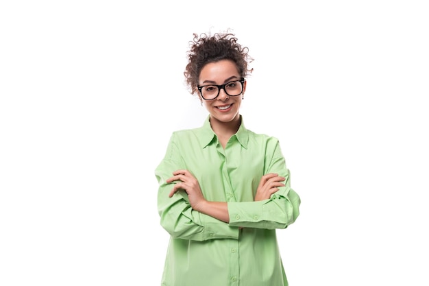 Pretty joven morena mujer rizada con gafas está vestida con una camisa verde sobre un fondo blanco con