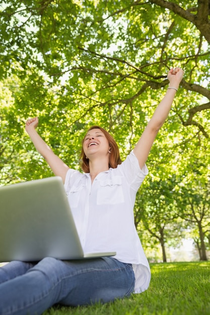 Pretty redhead usando seu laptop no parque e torcendo