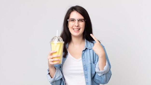 Pretty Woman sonriendo con confianza apuntando a su propia amplia sonrisa y sosteniendo un batido de vainilla