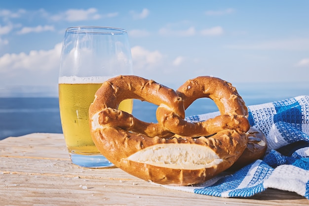 Pretzel alemán y vaso de cerveza en la luz del sol contra el cielo azul