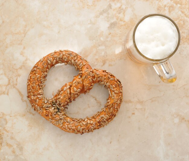 Pretzel alemão polvilhado com sementes e uma caneca de cerveja na mesa de mármore. vista do topo