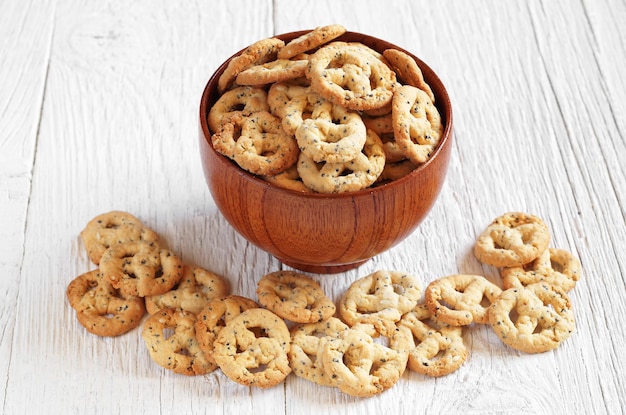 Pretzels com queijo e sementes em tigela na mesa de madeira branca Lanche salgado para cerveja