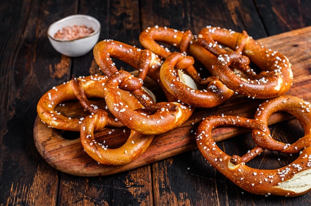 Pretzels macios caseiros com sal em uma placa de madeira. Fundo de madeira escuro. Vista do topo.