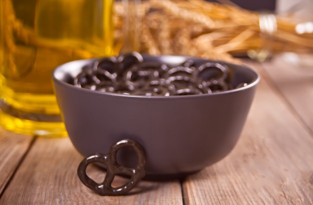 Pretzels pretos pequenos em uma tigela com cerveja de vidro ob na mesa de madeira.