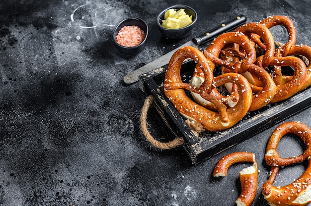 Pretzels salados horneados de Baviera en una bandeja de madera. Fondo negro. Vista superior. Copie el espacio.