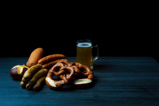 Pretzels, salchichas y cerveza en la mesa de madera y estilo de comida oscura Oktoberfest