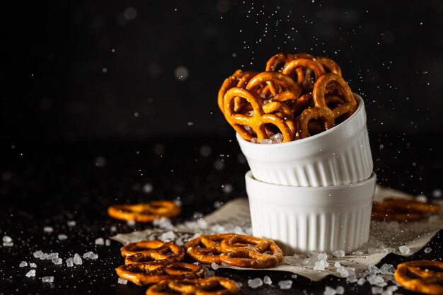 Los pretzels yacen en dos tazas sobre un fondo oscuro. Se vierte una gran cantidad de sal sobre el bretzel y se esparce.