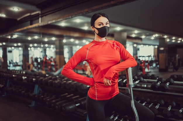 Prevenção de coronavírus covid-19, garota fitness com uma máscara médica segurando um haltere. Combate a vírus.