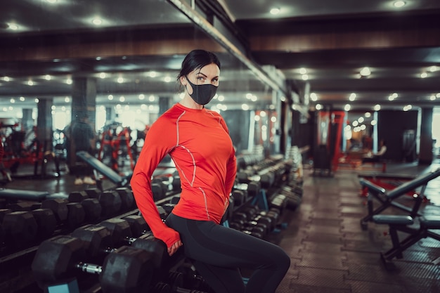 Prevenção do coronavírus covid-19, garota fitness com máscara médica posando no ginásio