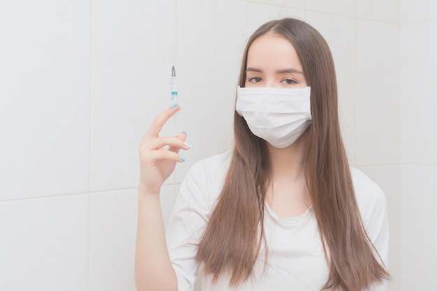 Prevención y protección contra la infección por virus La doctora con mascarilla y guantes sostiene una jeringa con una vacuna