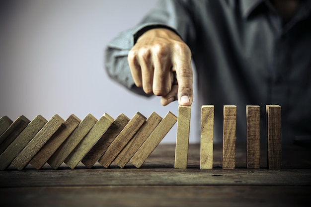 Prevenir manualmente la caída de la pila de torres de bloques de madera o el concepto de dominó de prevención de negocios financieros y gestión de riesgos o planificación estratégica