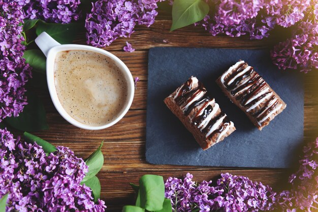 Primavera y desayuno recién hecho en una mesa de madera. Sobre la mesa hay lilas, pasteles y un capuchino. Un ramo de lilas sobre una mesa de madera.