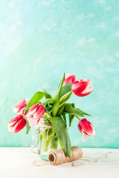 Primavera . Florece tulipanes en un tarro de cristal, en un blanco azul claro y de madera.