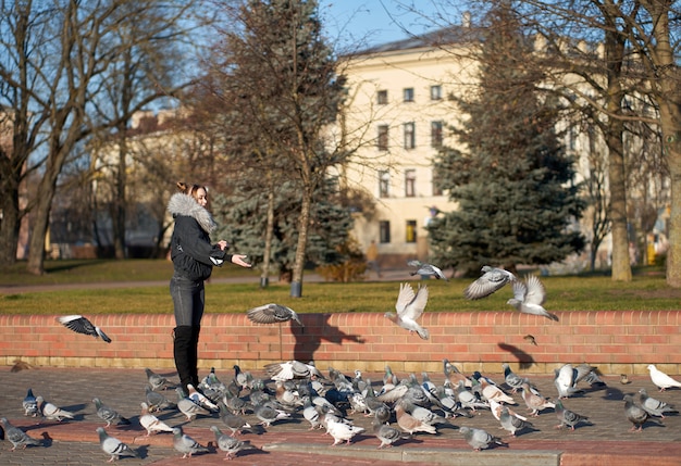 Primavera. Garota loira atraente elegante vestindo roupas elegantes, alimentando pombos de mãos na Praça da cidade.