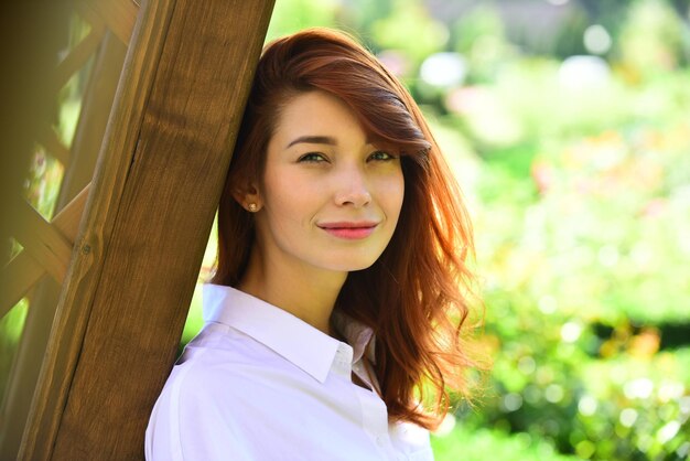 Primavera Hermosa chica pelirroja romántica en vestido de encaje blanco de pie cerca de árbol floreciente. Mujer en el jardín.