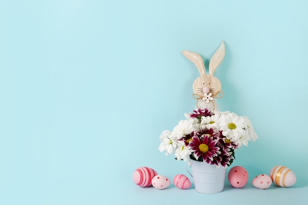 Primavera de Pascua azul con flores, conejito de madera y huevos rosados