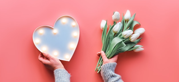 La primavera plana geométrica yacía con panel de luz en forma de corazón y flores de tulipán blanco sobre fondo rosa