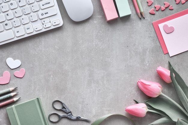 Primavera plana con teclado, ratón, tulipanes rosados, papelería, tarjetas de felicitación y corazones decorativos