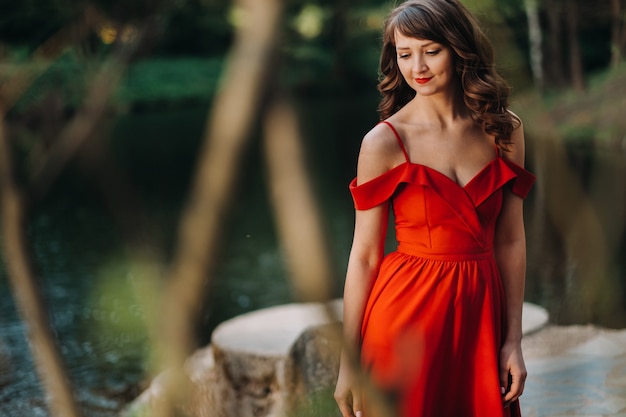 Primavera retrato de uma menina rindo em um longo vestido vermelho com cabelo comprido, caminhando no parque na floresta