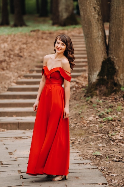 Primavera retrato de uma menina rindo em um longo vestido vermelho com cabelo comprido, caminhando no parque na floresta