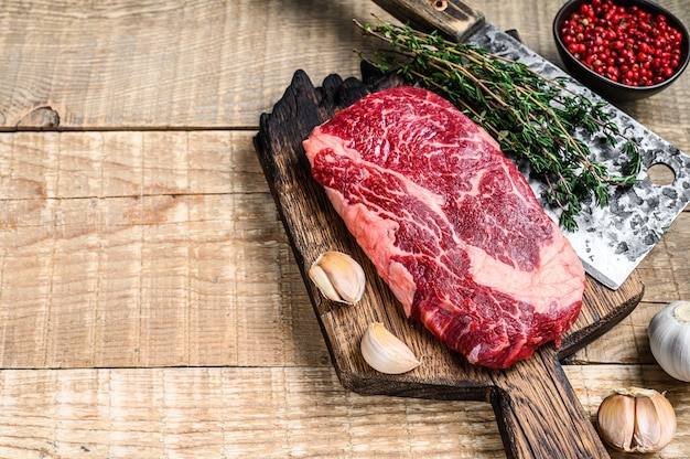 Prime Rib Eye rohes Rindfleisch Fleischsteak auf einem Metzger Holz Schneidebrett mit Hackmesser.