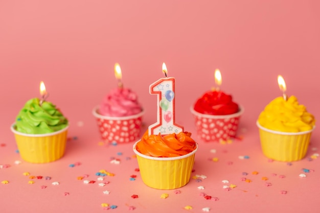 Primeira vela número 1 do bolo de aniversário em um cupcake entre bolos coloridos no fundo rosa