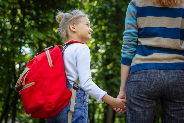 Primeiro dia na escola. Mulher e menina com mochila vermelha nas costas. Início das aulas. Primeiro dia de outono. Volta ao conceito de escola.