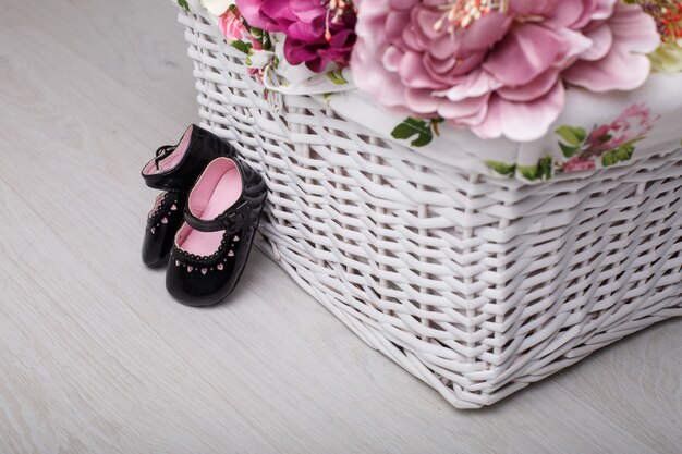 Primeiros sapatos para princesinha isolada na parede de luz com espaço para texto. sapatos de bebê de couro preto com flores de cesta de vime. sapatos elegantes para menina recém-nascida para os primeiros passos fechar.