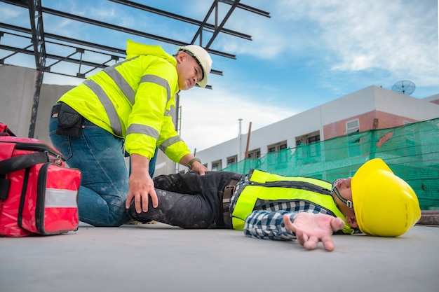 Primeiros Socorros em Acidentes de Emergência em Canteiros de Obras. Trabalhador da construção civil ficou ferido em uma queda de altura em um canteiro de obras. Os engenheiros ajudam os primeiros socorros, a equipe de segurança ajuda os funcionários a acidentes.