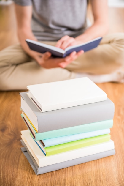 Primer del adolescente que se sienta en suelo cerca de la pila de libros.