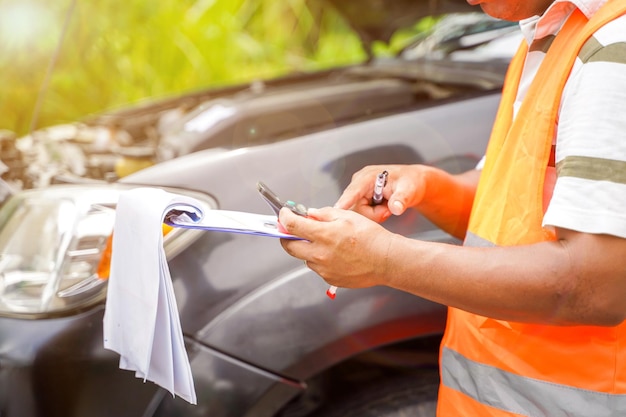 Primer y agente de seguros de cosechas escribiendo en el portapapeles mientras examina el automóvil después de un reclamo de accidente