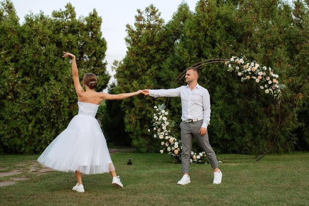 El primer baile del novio y la novia con un vestido de novia corto en un prado verde