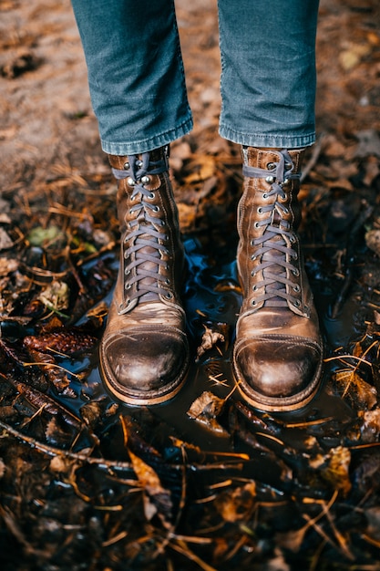 Primer de las botas rasguñadas viejas del vintage de las piernas del `s del hombre que se colocan en charco.