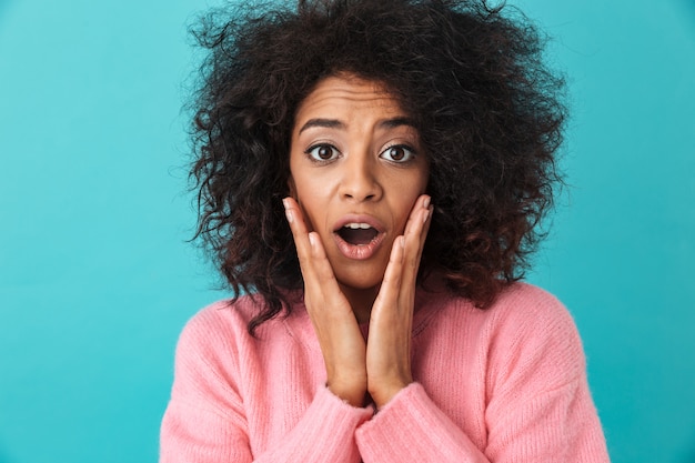 Primer colorido de la imagen de la mujer sorprendida agarrando la cara con mirada emocionada y boca abierta, aislado sobre la pared azul