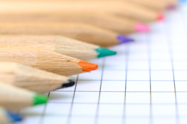 Primer conjunto de lápices multicolores en la hoja de papel a cuadros del cuaderno para el dibujo.