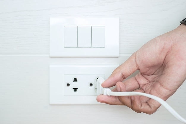 Primer dedo masculino desenchufar o enchufar el dispositivo de electricidad en la pared blanca en casa.