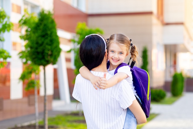 El primer día de clases, una madre lleva a una colegiala en sus brazos al primer grado el primer día de otoño, el concepto es volver a la escuela.